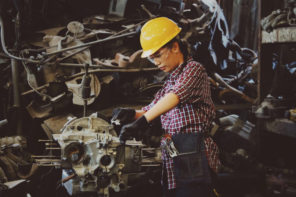 Начало Woman engineer wearing safety gear, working on machine repair in an industrial setting.