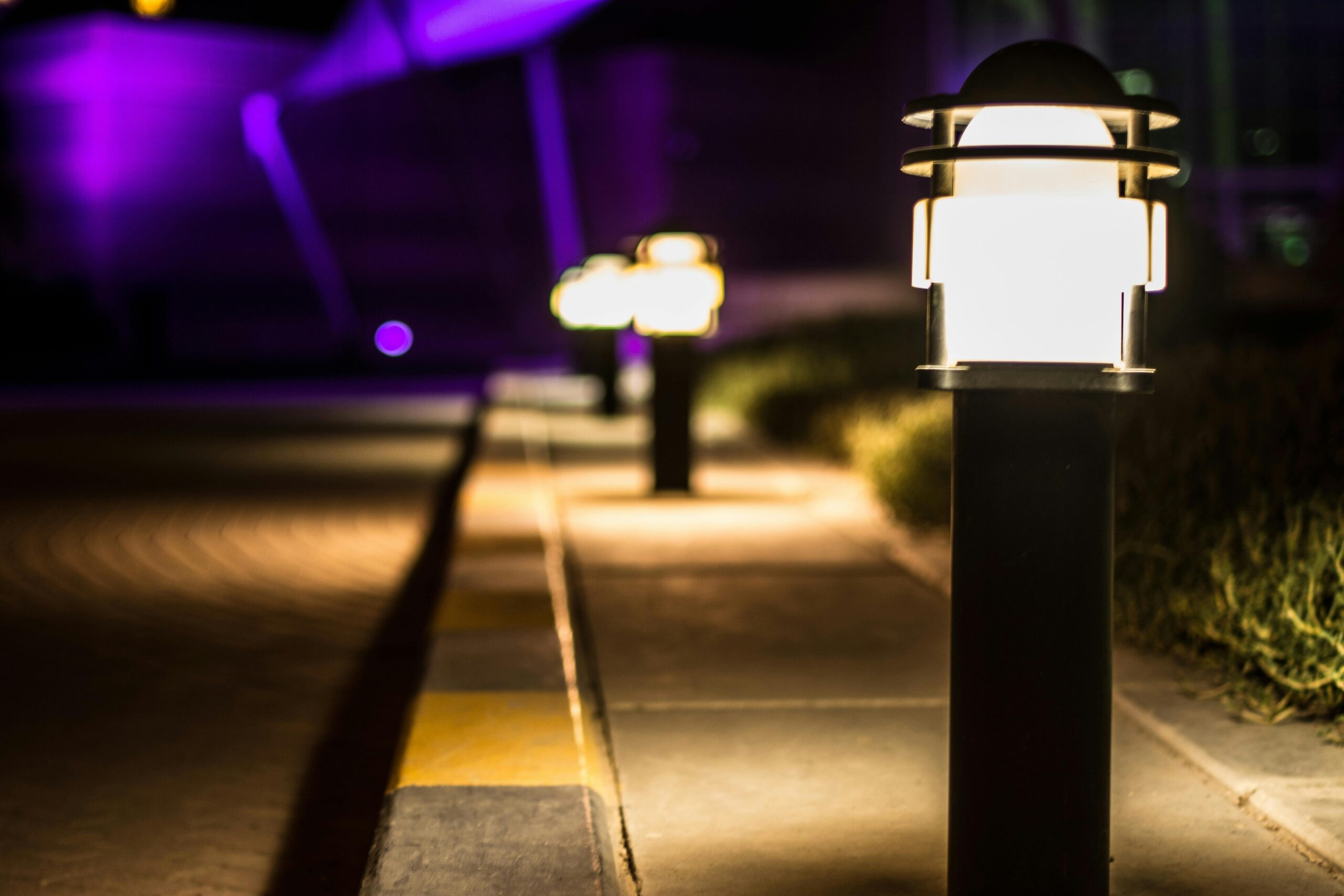 Начало A scenic night view of illuminated lamp posts lining a paved path with a bokeh effect.