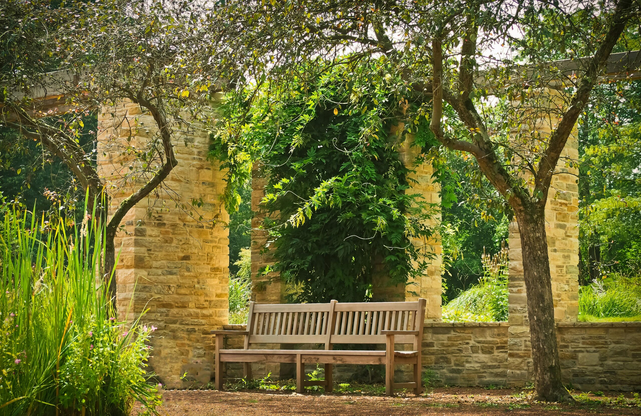 A tranquil park bench set under a stone archway surrounded by lush greenery and trees.